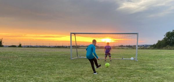 Zwei Kinder spielen Fußball vor einem Sonnenuntergang.